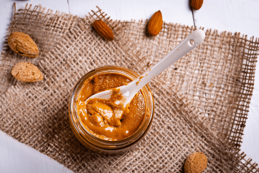 Almond Butter in a jar with a spoon inserted sitting on burlap