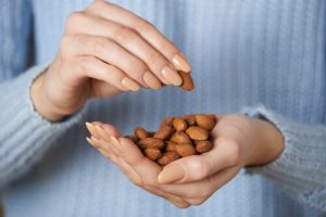 woman in blue sweater holding a hand full of almonds