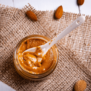 Almond Butter in a jar with a spoon inserted sitting on burlap